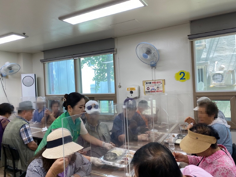 하당동 새마을부녀회 봉사자가 식당에서 장애인들에게 식판 음식을 배식하는 모습. 투명 칸막이가 설치된 식탁에서 모두가 식사를 준비하고 있다.