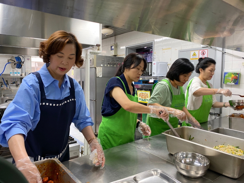 목련회 봉사자들이 주방에서 위생장갑을 끼고 반찬을 식판에 나누어 담으며 배식 준비를 하는 모습