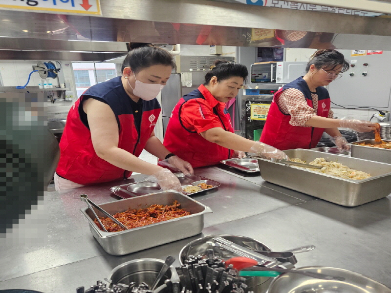 목련로터리클럽 봉사자들이 빨간 조끼를 입고 주방에서 반찬을 식판에 나누어 담는 모습