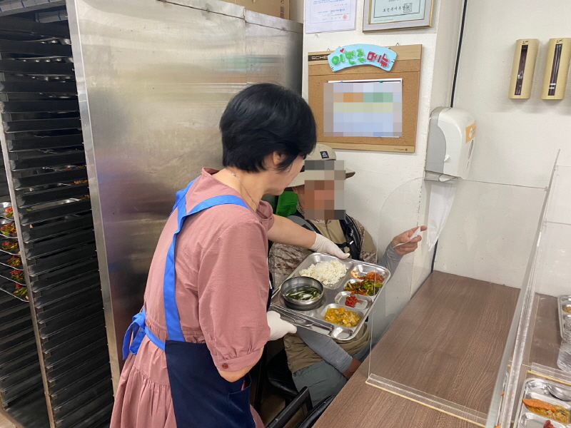 민주당 여성위원회 자원봉사자가 밥과 국, 반찬이 담긴 식판을 어르신에게 전달하는 장면