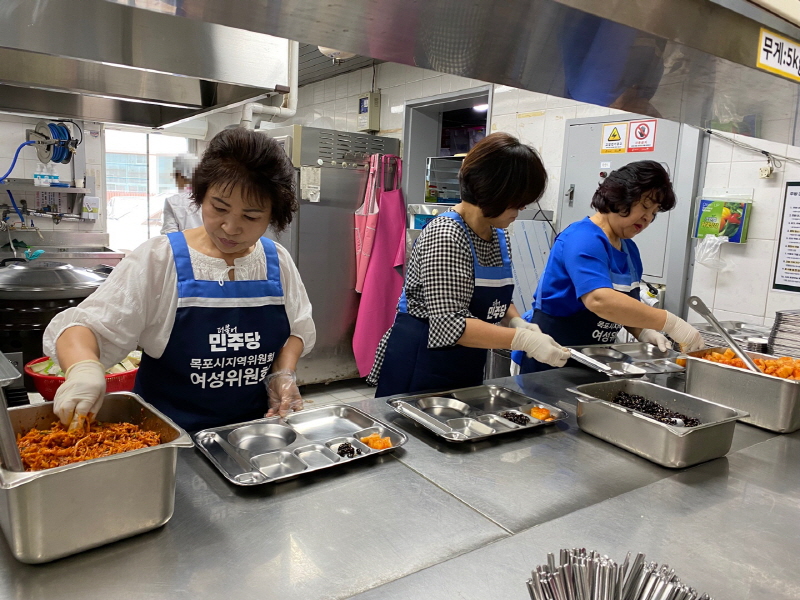 민주당 여성위원회 봉사자들이 주방에서 반찬을 식판에 담으며 배식 준비를 하고 있는 모습