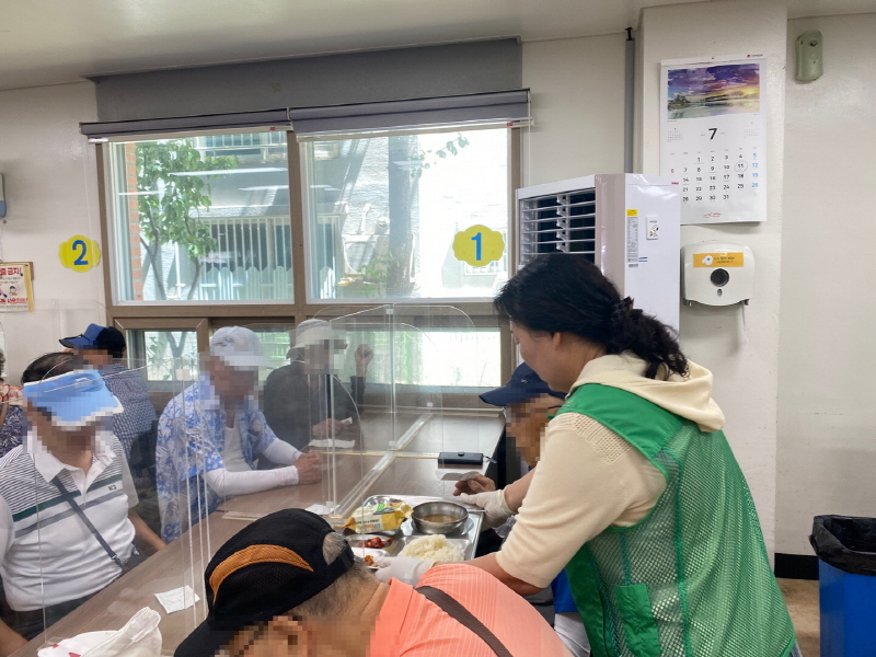 하당동 새마을부녀회 봉사자가 초록색 조끼를 입고 장애인에게 밥과 반찬이 담긴 식판을 나누어주는 모습