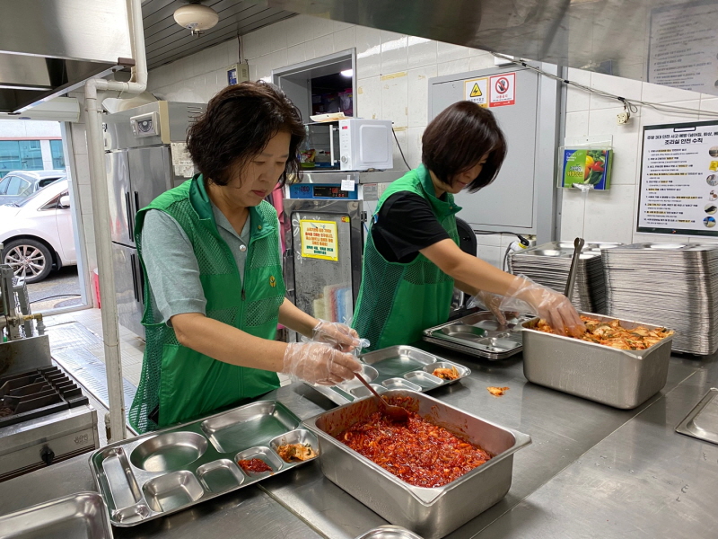 하당동 새마을부녀회 자원봉사자 두 명이 급식소 주방에서 장갑을 끼고 반찬을 식판에 담는 모습