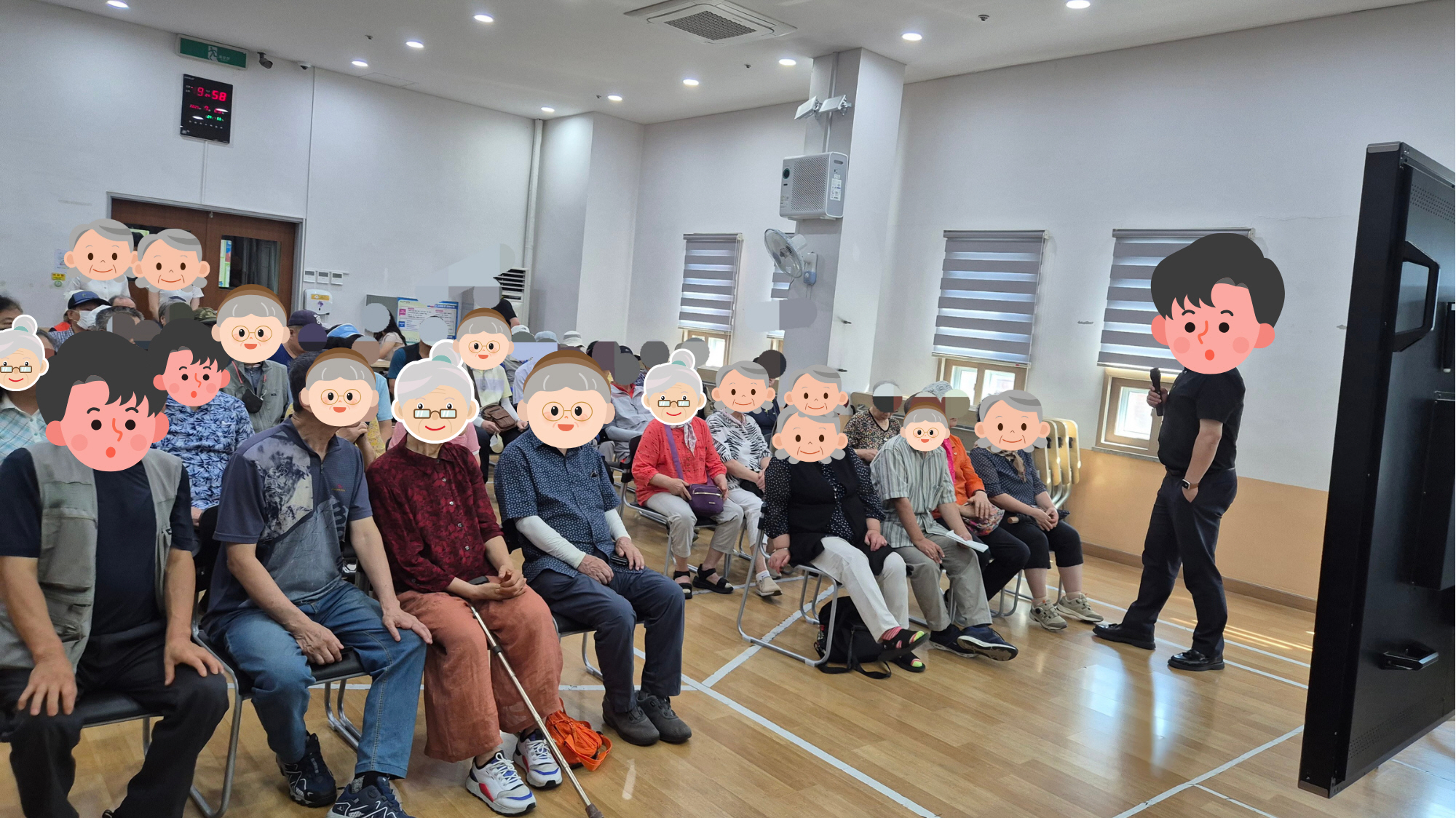 강사가 앞에서 마이크를 들고 설명하는 가운데, 참가자들이 의자에 앉아 강사의 안내를 경청하고 있습니다. 여러 명이 전면을 바라보며 집중하는 모습이 보입니다