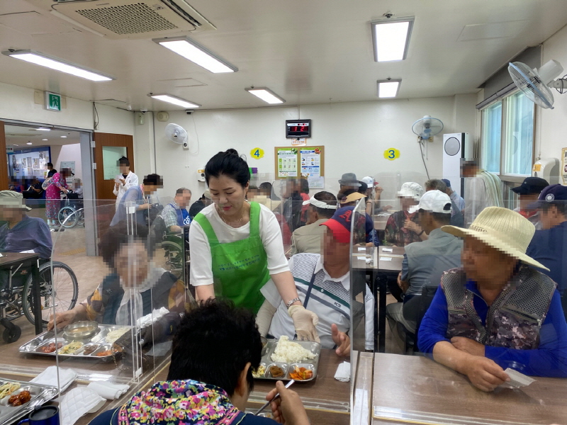 목련회 봉사자가 복지관 식당에서 많은 장애인들에게 식판을 나누어주는 모습. 투명 칸막이가 설치되어 있다