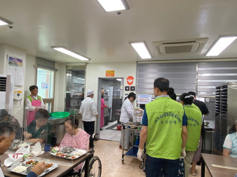 국제피플투피플 목포챕터 봉사자들이 초록색 조끼를 입고 장애인들에게 음식을 배식하는 모습. 식당 안은 분주한 분위기다