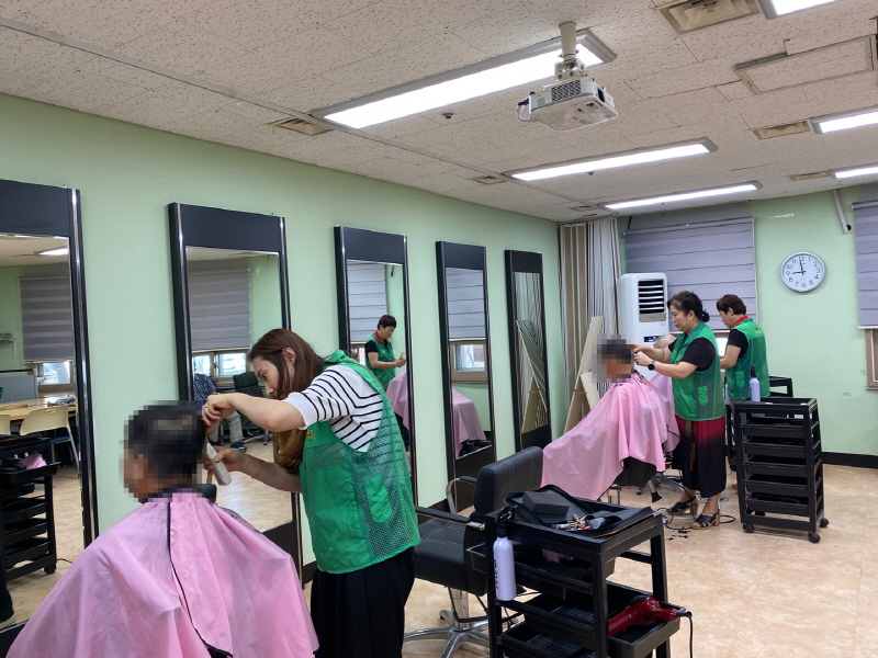 초록색 조끼를 입은 하당동새마을부녀회 봉사자들이 거울 앞에서 남성 이용자들의 머리를 손질하고 있는 모습