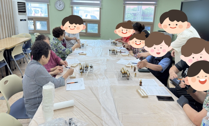 여러 명의 이용자들이 복지관 강의실 긴 테이블에 앉아 아로마 방향제 만들기 활동에 참여하고 있다. 작은 병과 스포이드, 재료들이 놓여 있으며, 직접 조향하며 향기를 담는 과정을 체험하는 모습이다