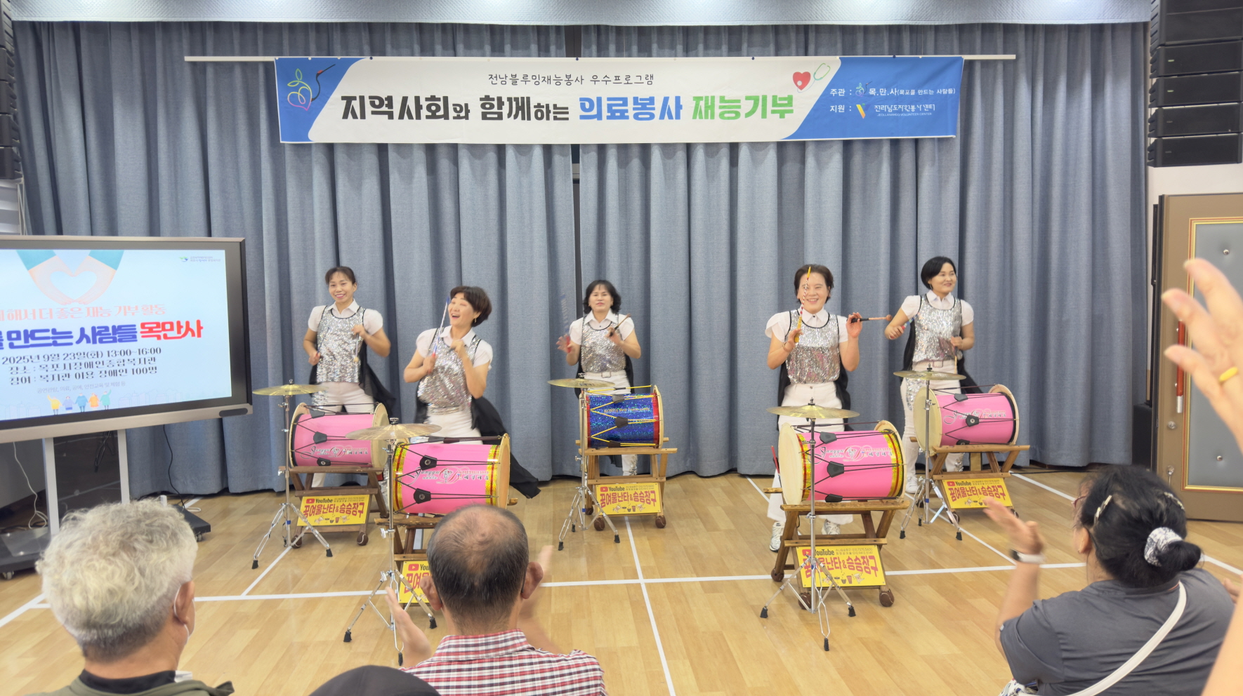 승승장구 여성 난타 공연팀이 무대에서 장구와 북을 치며 공연을 하고 있다. 무대 앞에서 관객들이 박수를 치며 공연을 즐기고 있다.