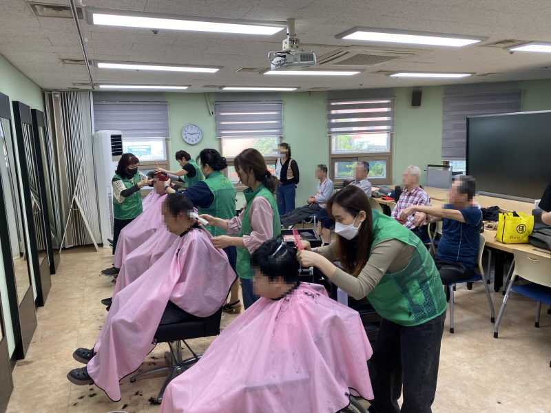 하당동새마을부녀회 봉사자들이 이용고객들의 머리를 다듬는 모습으로, 뒷자리에는 차례를 기다리는 사람들이 앉아 있다