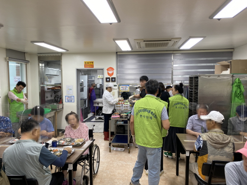 (사)국제피플투피플 목포챕터 봉사자들이 배식 봉사를 하는 가운데, 휠체어를 이용하는 고객을 포함해 다양한 사람들이 식탁에서 식사하는 모습