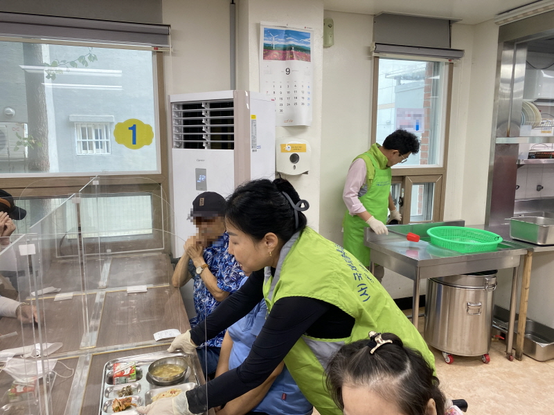 (사)국제피플투피플 목포챕터 봉사자가 식당에서 앉아 있는 고객에게 음식을 전달하는 장면. 식당 내부에는 9월 달력이 걸려 있음