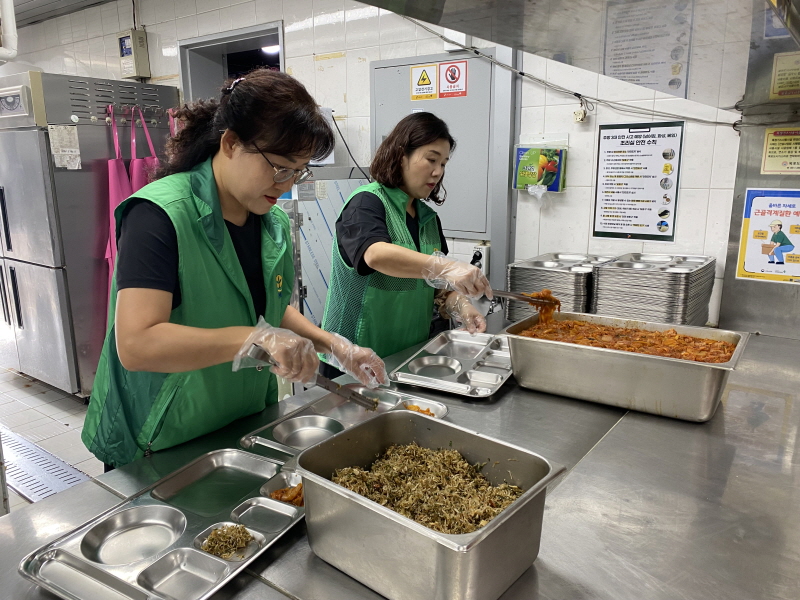 하당동새마을부녀회 봉사자 두 명이 주방에서 위생장갑을 끼고 스테인리스 식판에 나물을 담고 있는 모습