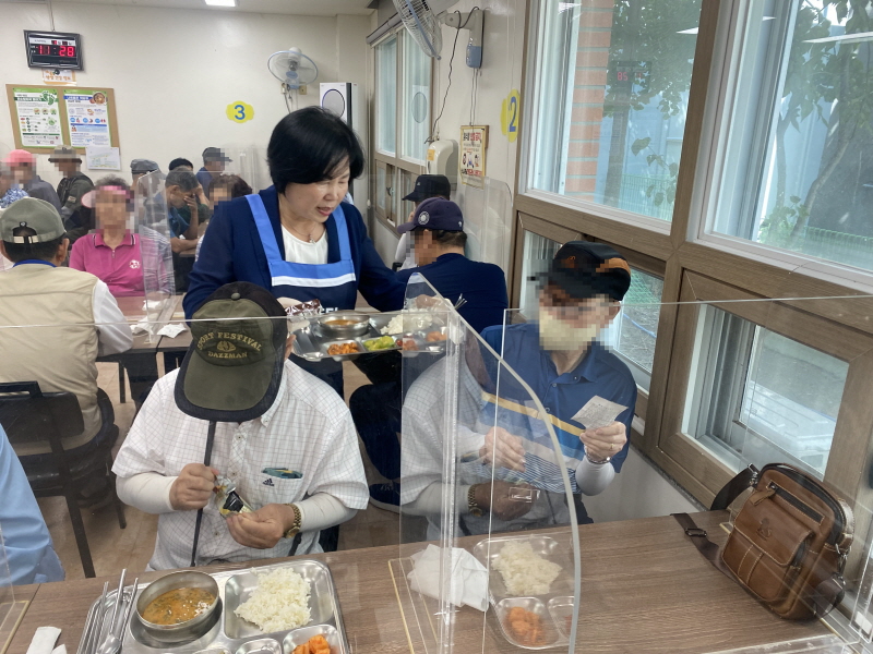 민주당여성위원회 봉사자가 식당에서 앉아 있는 남성 고객에게 음식을 전달하는 장면. 식탁마다 투명 가림막이 설치되어 있음
