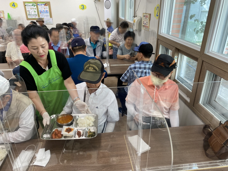 목포시청 공직자 부인회 봉사자가 식당에서 앉아 있는 이용고객에게 식판을 나눠주는 장면. 고객들이 식사를 기다리고 있음