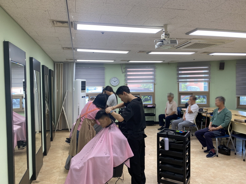 청담헤어 봉사자들이 의자에 앉은 이용고객들의 머리를 손질하고 있고, 대기 중인 사람들이 옆자리에 앉아 순서를 기다리고 있다