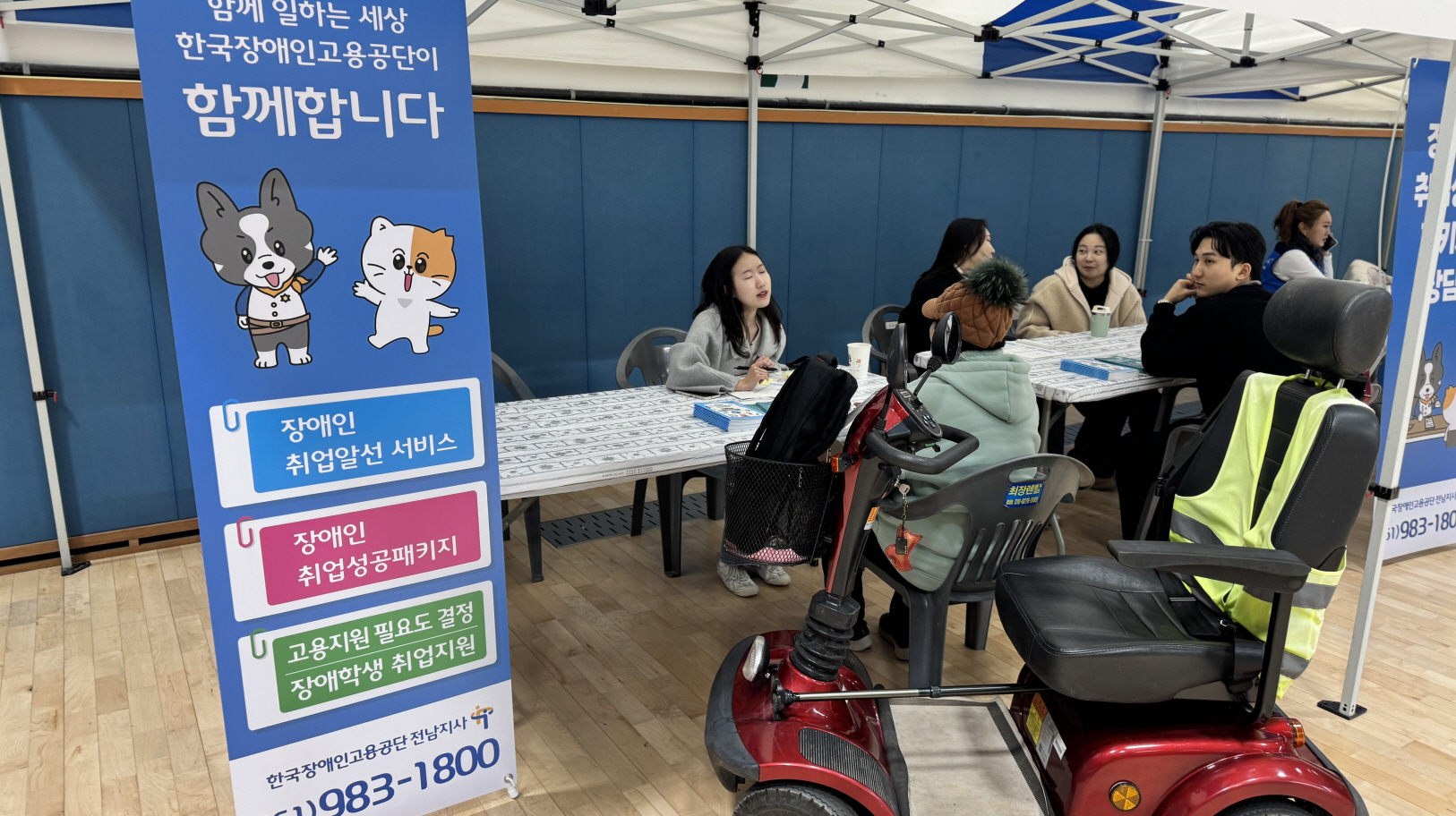 실내 체험 부스에서 한국장애인고용공단 전남지사 직원이 테이블에 앉아 장애인 참가자와 마주 보고 직업상담을 진행하고 있으며, 옆 파란 배너에 장애인 취업지원 서비스 안내 문구가 적혀 있는 모습.