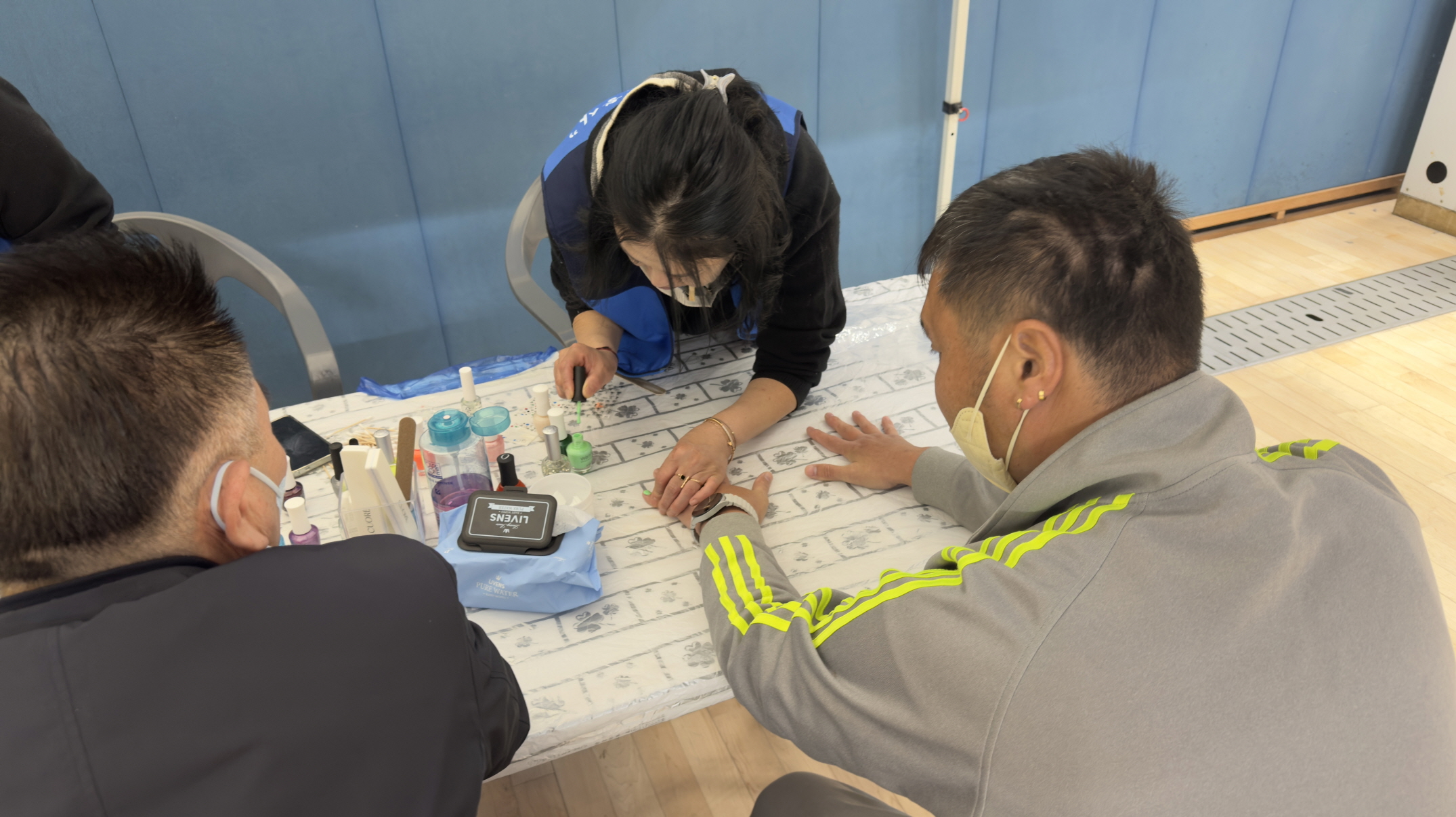 테이블 위에 매니큐어와 도구들이 놓여 있고, ‘목포를 만드는 사람들’ 봉사자가 장애인 참가자의 손을 잡고 초록색 매니큐어를 바르며 네일아트 서비스를 제공하는 장면.