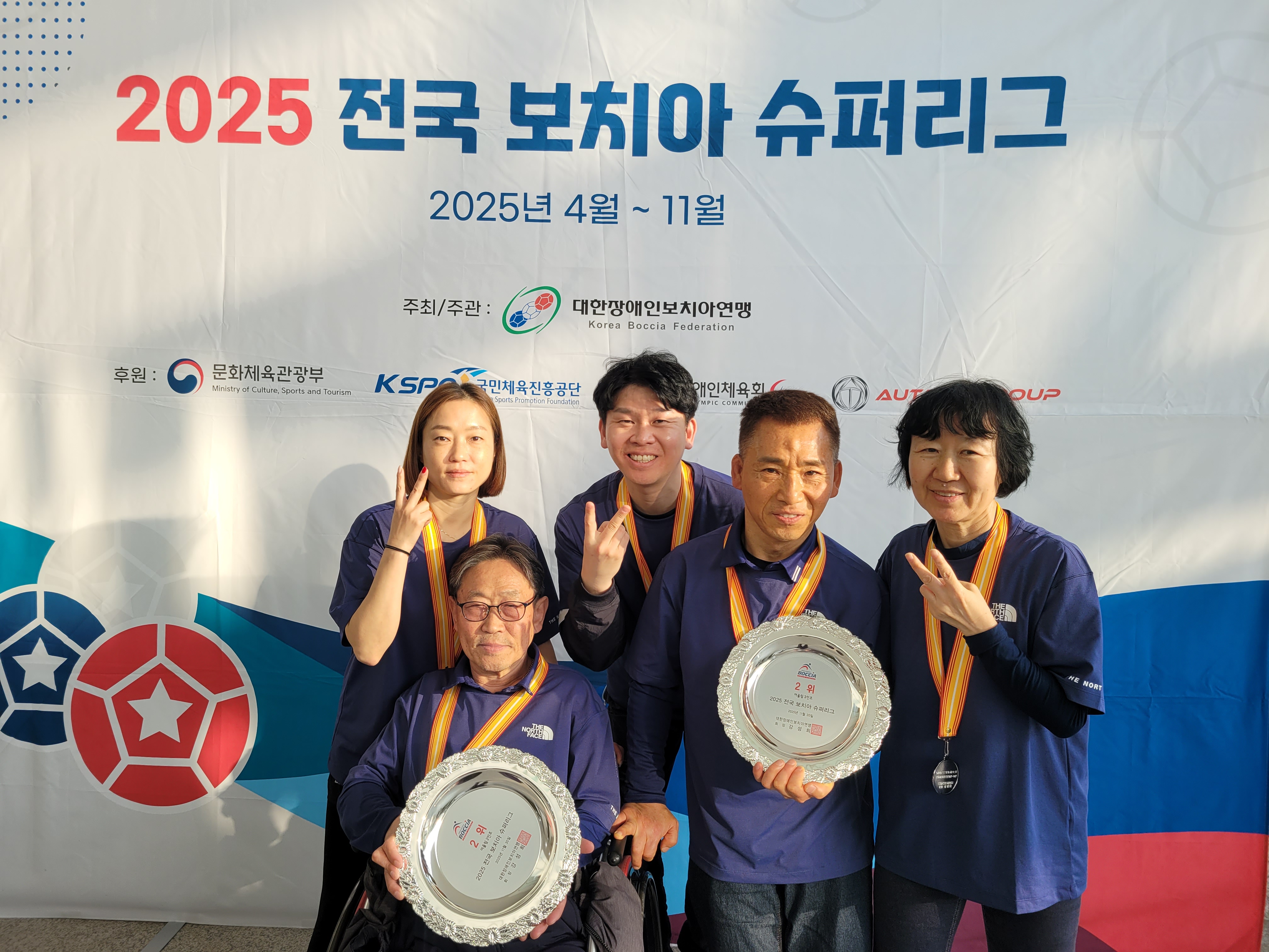 ‘2025 전국 보치아 슈퍼리그’ 현수막 앞에서 목포시장애인종합복지관 보치아 생활체육클럽 선수 5명이 메달을 목에 걸고 단체사진을 찍고 있다. 앞줄의 두 남성 선수는 각각 ‘2위’라고 적힌 은색 상패 접시를 들고 있고, 뒷줄의 세 사람은 손가락으로 V자를 그리며 기쁜 표정으로 포즈를 취해 어울림 부문 혼성 2인조·3인조 최종 2위 수상을 함께 축하하고 있다.