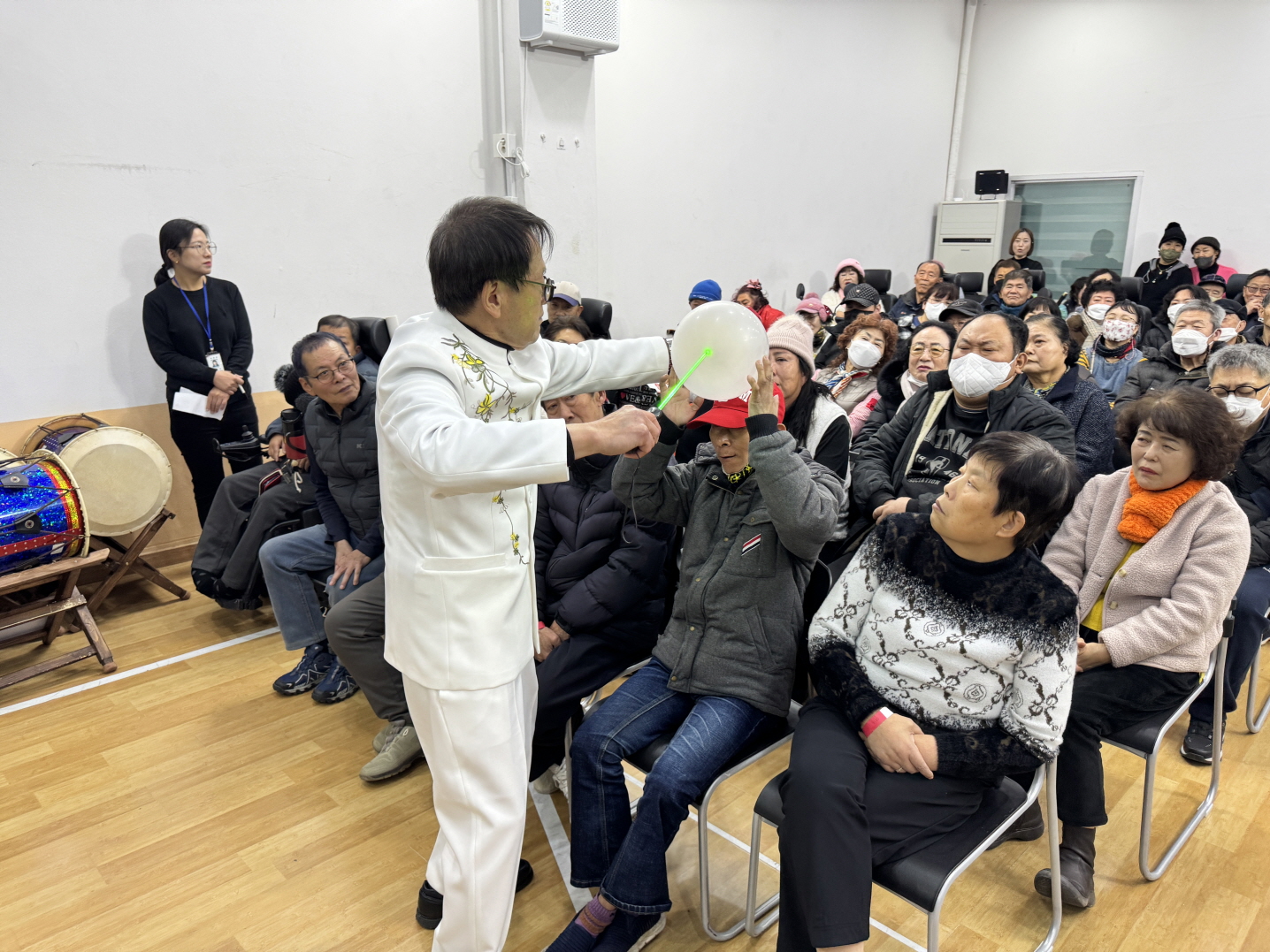 2025 송년감사행사 식전 마술공연에서 마술사가 무대 앞에서 풍선을 이용한 퍼포먼스를 선보이고, 객석의 이용고객들이 가까이에서 집중해 관람하며 일부는 손을 뻗어 참여하고 있다.