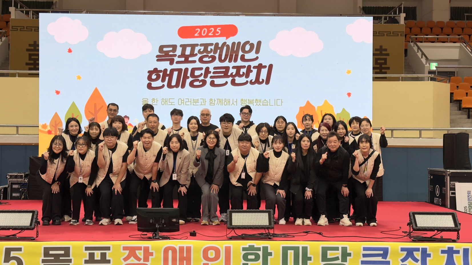 지역사회 공헌활동으로 진행된 ‘2025 목포장애인 한마당큰잔치’ 현장에서 복지관 직원들이 무대 앞에 모여 단체로 기념촬영을 하는 모습. 무대 뒤 대형 화면에는 “2025 목포장애인 한마당큰잔치” 문구가 표시되어 있다.