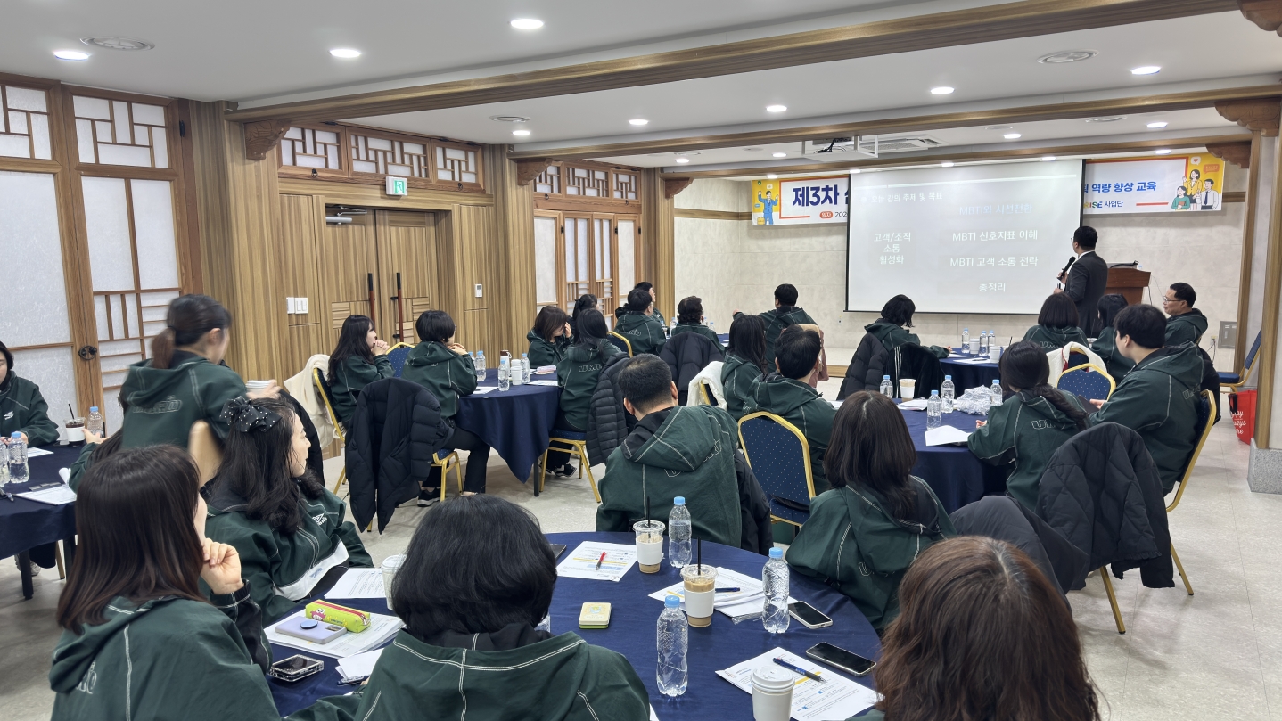 MBTI를 활용한 조직활성화 및 고객소통 교육 전경. 강당 스크린에 'MBTI와 시설경영' 강의안이 띄워져 있으며, 초록색 단체복을 입은 직원들이 원형 테이블에 둘러앉아 집중하고 있다.