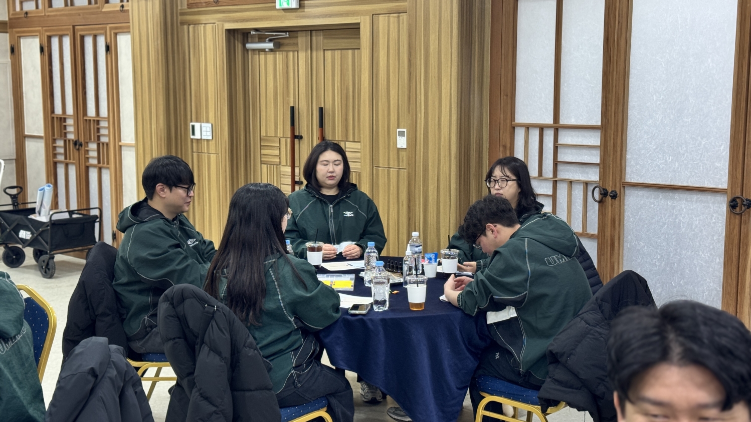 아로마 및 컬러테라피 체험 활동 전, 직원들이 원형 테이블에 둘러앉아 눈을 감고 차분하게 마음을 가다듬으며 명상에 잠겨 있는 모습.