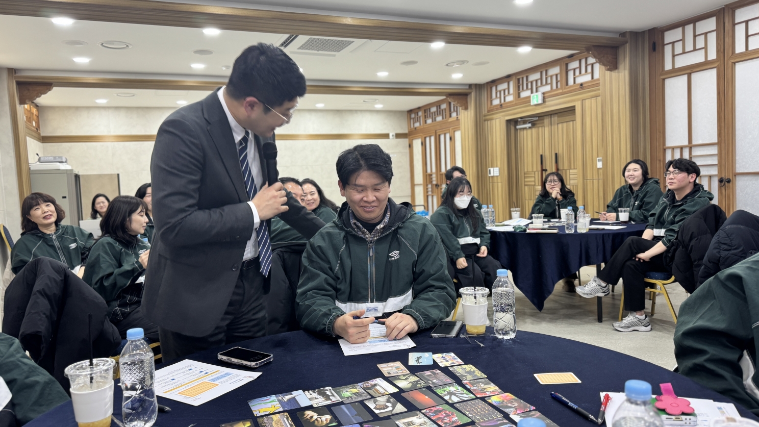 MBTI 교육 중 강사가 테이블로 다가가 직원과 소통하는 모습. 테이블 위에는 성격 유형 파악을 위한 그림 카드들이 펼쳐져 있다.