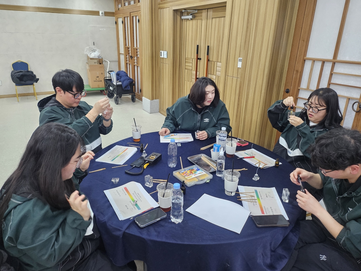 아로마 및 컬러테라피 체험 활동의 마지막 단계로, 직원들이 자신만의 향수를 직접 만드는 모습. 테이블 위에 놓인 다양한 향료와 스포이트, 유리병을 활용하여 향 배합 실습에 열중하고 있다.