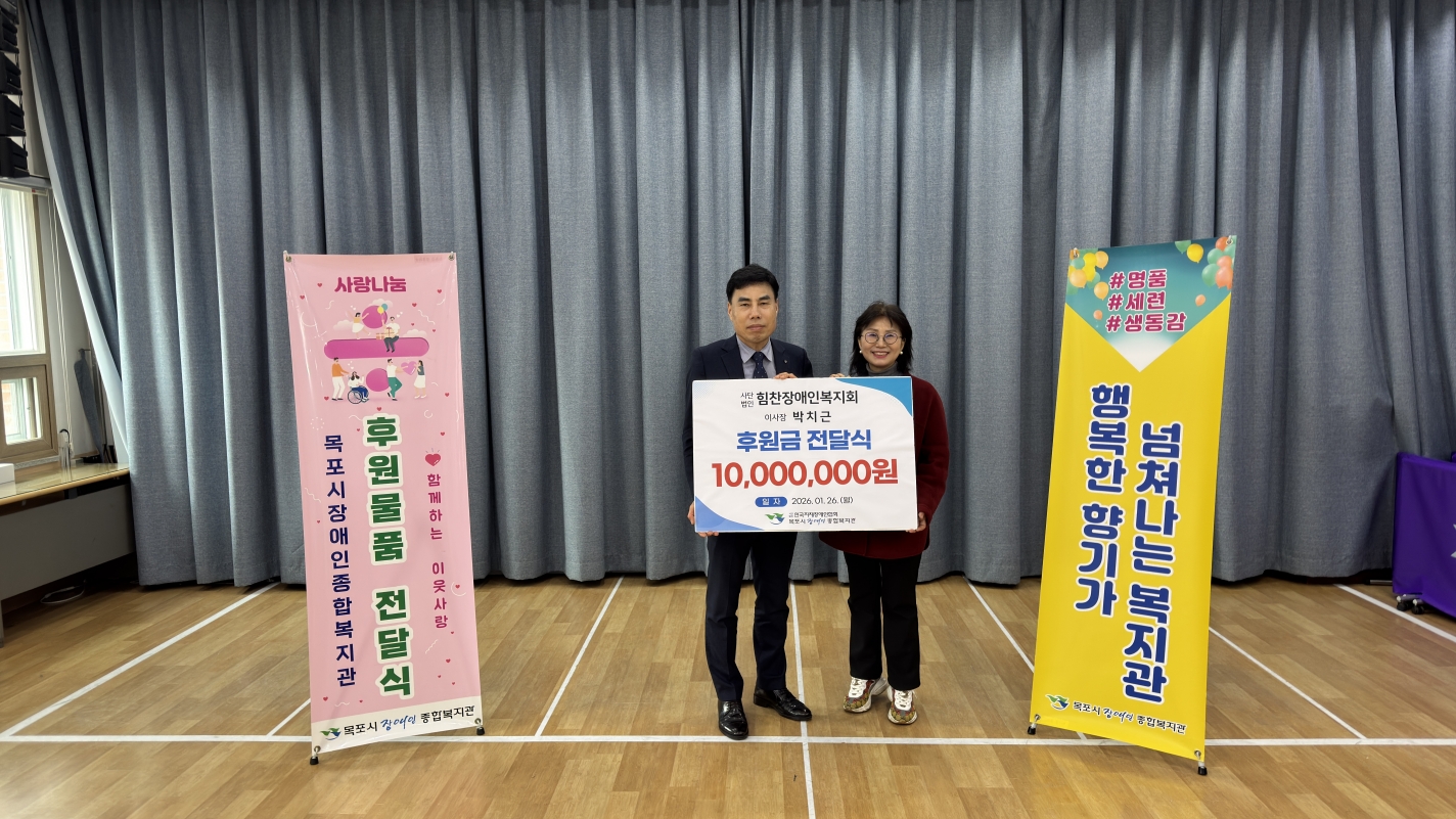 후원금 전달식에서 박치근 이사장과 복지관 대표가 기념 촬영을 하는 모습. 두 사람이 중앙에서 '사단법인 힘찬장애인복지회 이사장 박치근, 후원금 전달식 10,000,000원'이라고 적힌 기부 판넬을 나란히 들고 환하게 웃고 있습니다. 배경으로는 회색 커튼과 행사 안내 배너가 배치되어 있습니다.