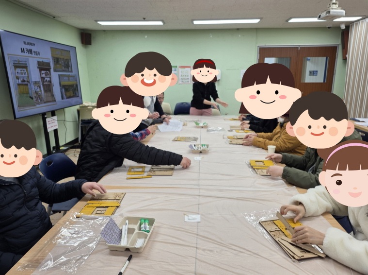 강의실 내 커다란 테이블에 둘러앉은 사람들이 TV 화면의 안내에 따라 종이 또는 나무 조립 키트를 활용해 모형 만들기 체험을 하고 있는 모습